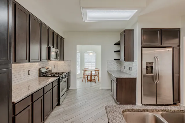 a kitchen with stainless steel appliances granite countertop a refrigerator a stove and a sink with wooden floor