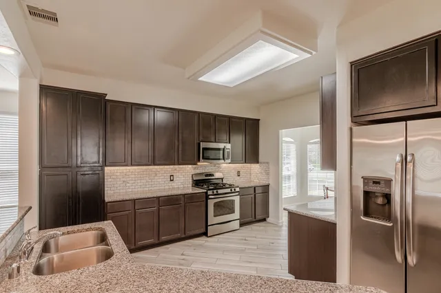 a kitchen with stainless steel appliances granite countertop a refrigerator a stove and a sink with wooden floor