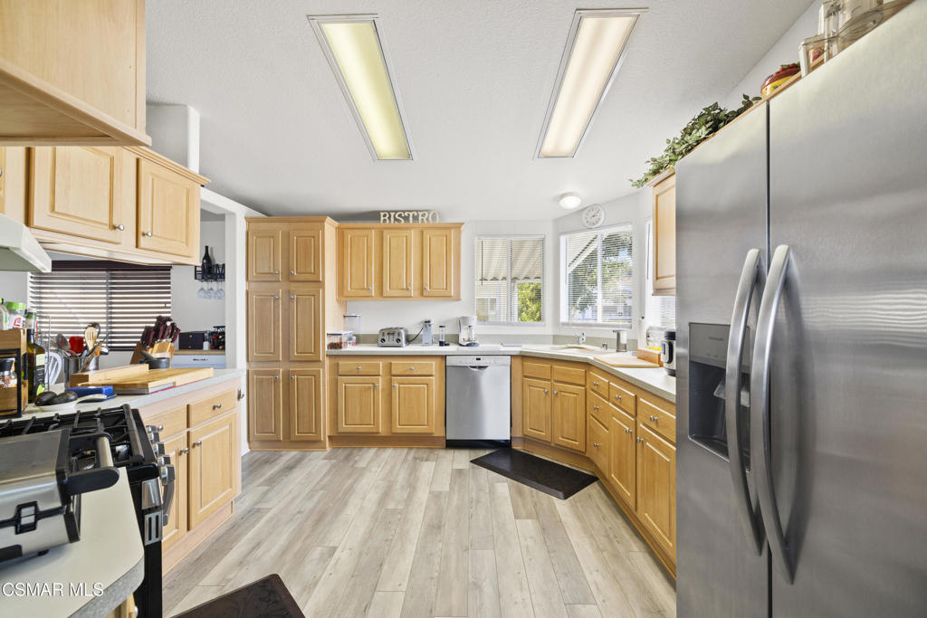 195 Tierra Rejada Road, Unit 52 Simi Valley, CA 93065 - Photo 12 of 34 a kitchen with a refrigerator a sink dishwasher a stove and white cabinets with wooden floor