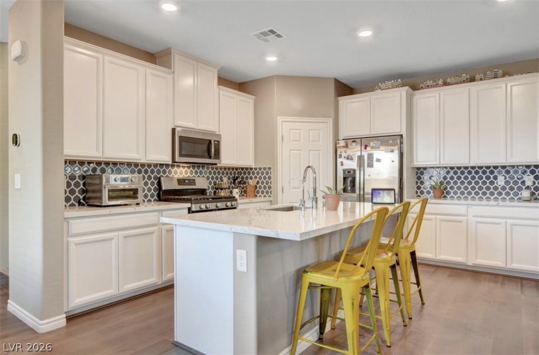 6920 Fossil Rim Street North Las Vegas, NV 89084 - Photo 2 of 9 A well-appointed kitchen showcasing white cabinetry, an island with seating, and a stylish tiled backsplash.