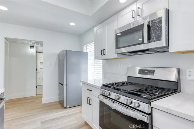 a kitchen with stainless steel appliances a sink dishwasher stove and white cabinets with wooden floor