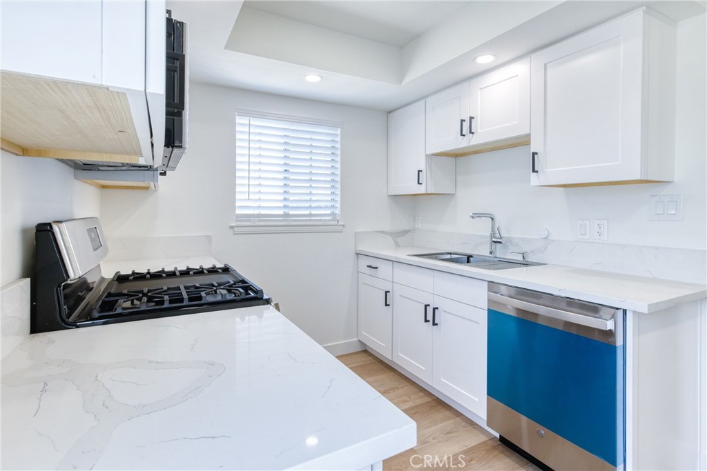320 West Truslow Avenue, Unit D Fullerton, CA 92832 - Photo 18 of 25 a kitchen with stainless steel appliances a sink dishwasher stove and white cabinets with wooden floor