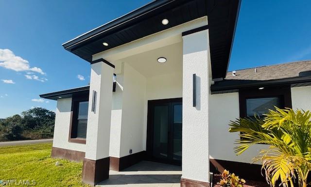165 Patio Street Lehigh Acres, FL 33974 - Photo 4 of 34 View of exterior entry featuring stucco siding and a yard