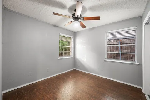 an empty room with wooden floor fan and windows