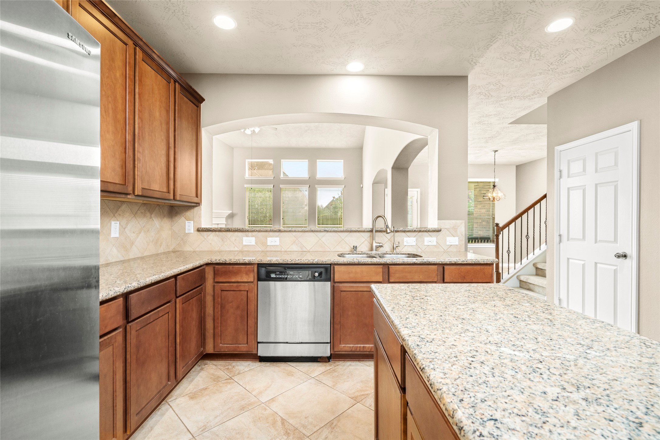 5307 Amber Sky Lane Rosharon, TX 77583 - Photo 21 of 50 This kitchen features granite countertops, wooden cabinetry, and stainless steel appliances. It opens to a bright living area with large windows and an arched pass-through, enhancing the spacious feel.