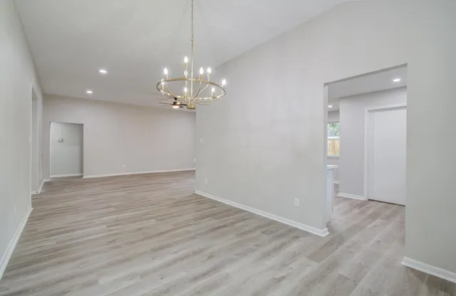 a view of an empty room with wooden floor and chandelier
