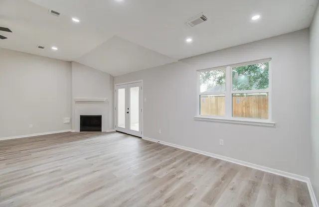 an empty room with wooden floor fireplace and windows