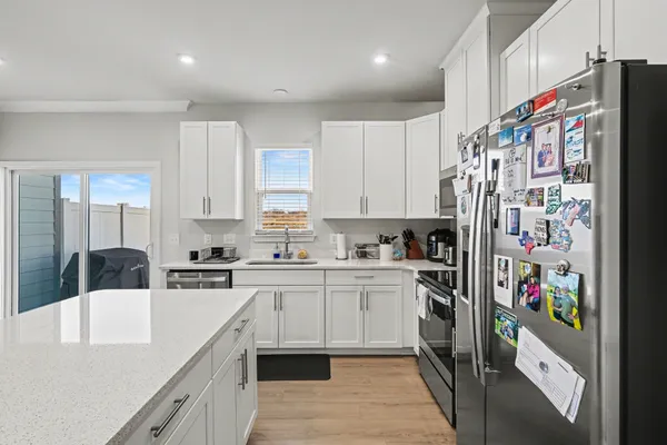 a kitchen with stainless steel appliances granite countertop a refrigerator a sink dishwasher and white cabinets with wooden floor