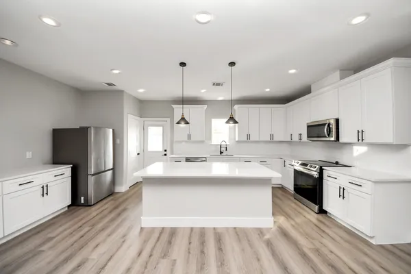 a large white kitchen with a white countertops a stove a sink and a refrigerator