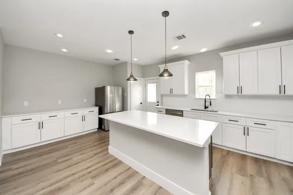 a large white kitchen with kitchen island a sink stainless steel appliances and white cabinets
