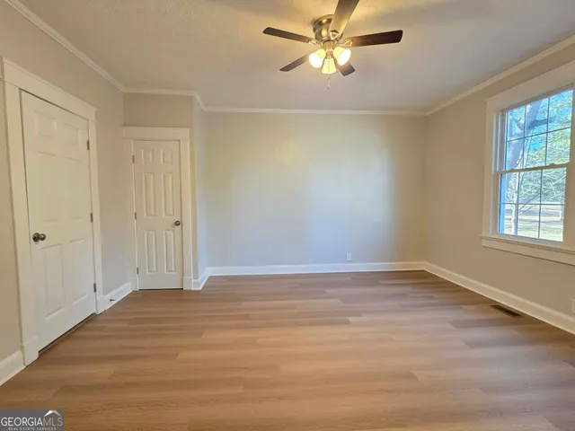 an empty room with wooden floor fan and windows