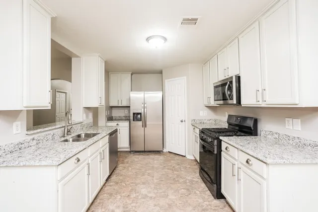 a kitchen with stainless steel appliances granite countertop a sink stove refrigerator and white cabinets with wooden floor