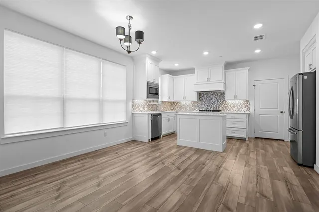 a kitchen with stainless steel appliances granite countertop a refrigerator a sink dishwasher a stove and white countertops with wooden floor