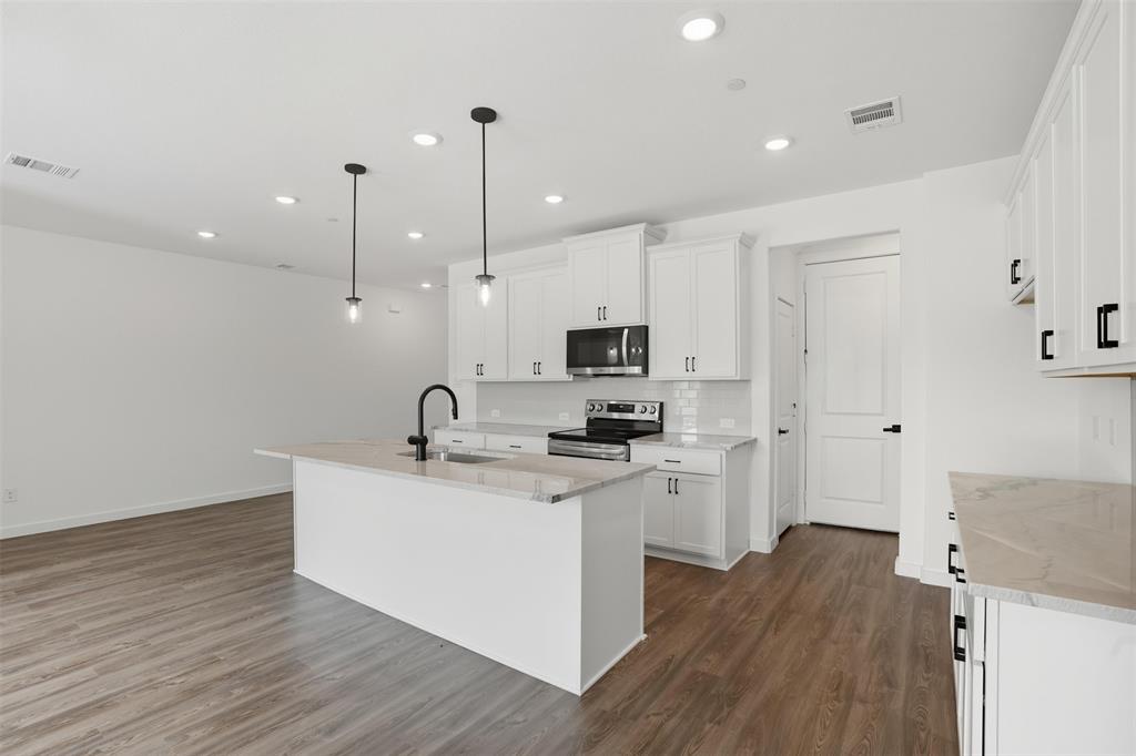 1606 Governors Boulevard Heath, TX 75126 - Photo 15 of 37 Kitchen with light stone countertops, a kitchen island with sink, white cabinets, decorative light fixtures, and stainless steel appliances
