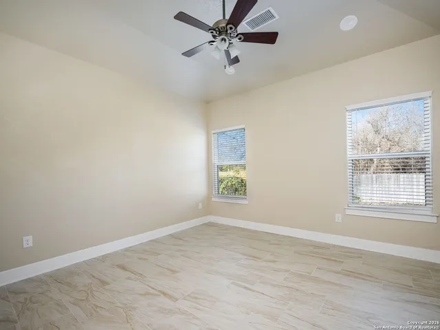 an empty room with wooden floor windows and fan