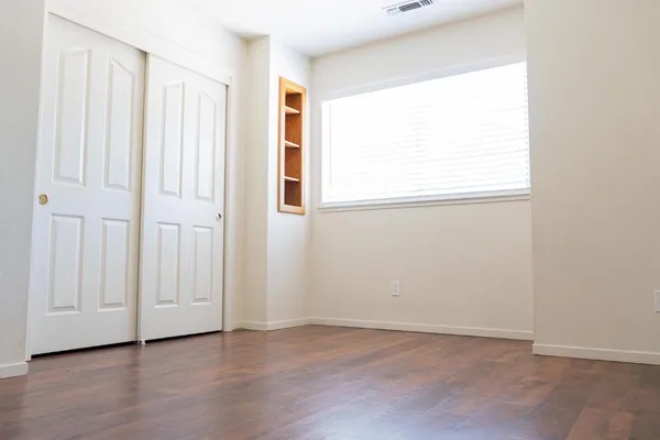 an empty room with wooden floor and windows with curtains