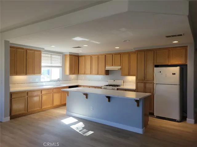 a kitchen with stainless steel appliances granite countertop a refrigerator a sink dishwasher a stove and white countertops with wooden floor