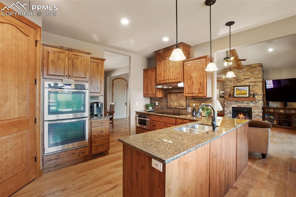 5070 Vessey Road Colorado Springs, CO 80908 - Photo 12 of 49 Kitchen featuring black electric stovetop, under cabinet range hood, double oven, a stone fireplace, and a sink