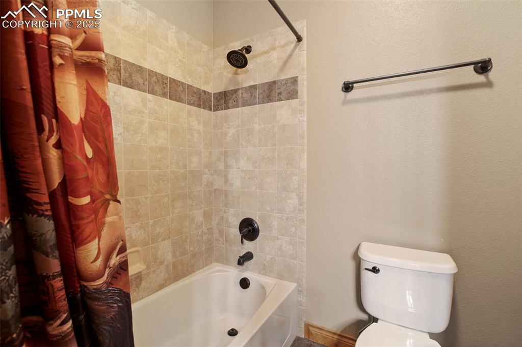 5070 Vessey Road Colorado Springs, CO 80908 - Photo 21 of 49 Bathroom with a textured wall, toilet, and shower / bath combination with curtain