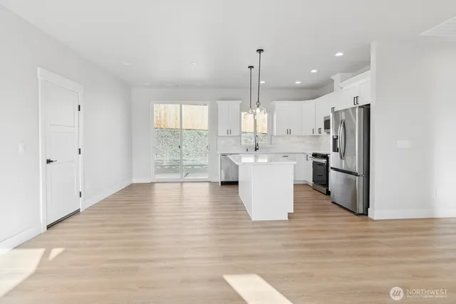 a open kitchen with stainless steel appliances granite countertop a refrigerator a sink dishwasher and white cabinets with wooden floor