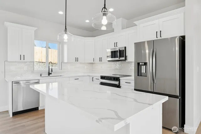 a kitchen with stainless steel appliances a sink a stove a refrigerator cabinets and wooden floor