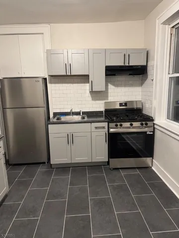 a white kitchen with granite countertop a stove a sink and a refrigerator