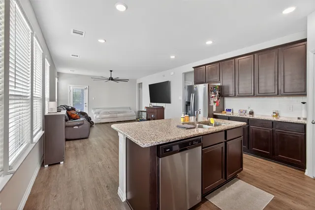 a kitchen with stainless steel appliances kitchen island granite countertop a sink dishwasher stove and refrigerator with wooden floor