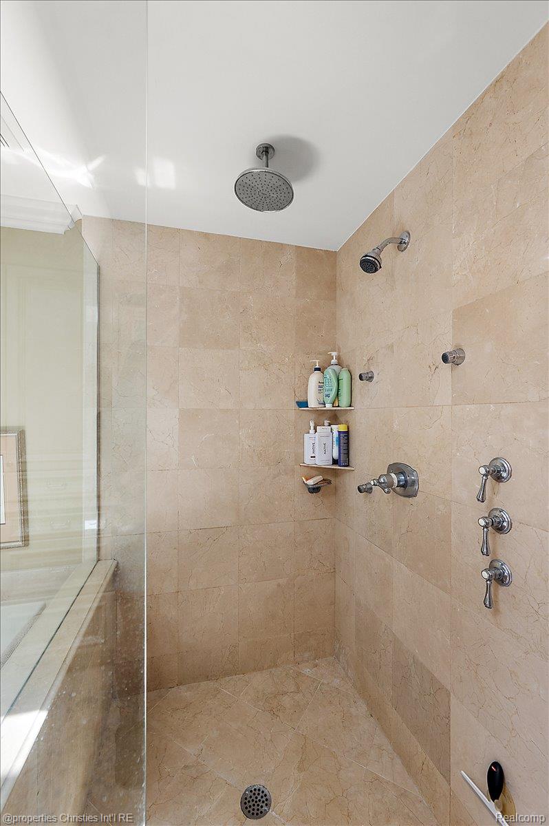 135 Clifton Road Bloomfield Hills, MI 48301 - Photo 42 of 77 Enclosed shower featuring stone-finish wall and floor tiles, a ceiling-mounted rainfall showerhead, a wall-mounted showerhead, and multiple chrome-finish body sprayers