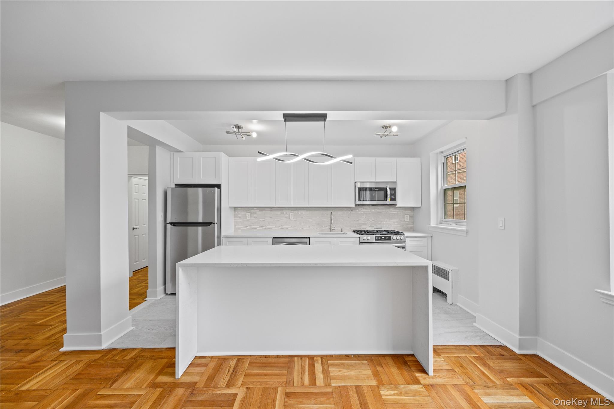 220 Pelham Road, Unit 1K New Rochelle, NY 10805 - Photo 1 of 1 Kitchen with stainless steel appliances, white cabinetry, a kitchen island, backsplash, and light stone countertops