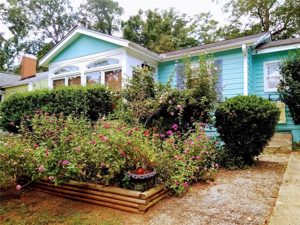 a house with a lot of flower plants sitting in front of house