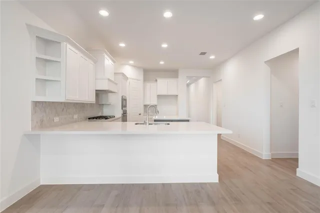 a large kitchen with kitchen island a sink a stove a refrigerator and white cabinets with wooden floor