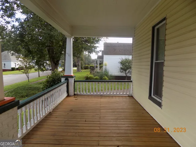 a view of a porch with wooden floor and bench in front of garden