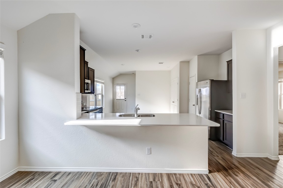 545 Greatest Gift Way Jarrell, TX 76537 - Photo 11 of 34 Kitchen with dark brown cabinetry, a peninsula, dark wood-style floors, vaulted ceiling, and a kitchen breakfast bar