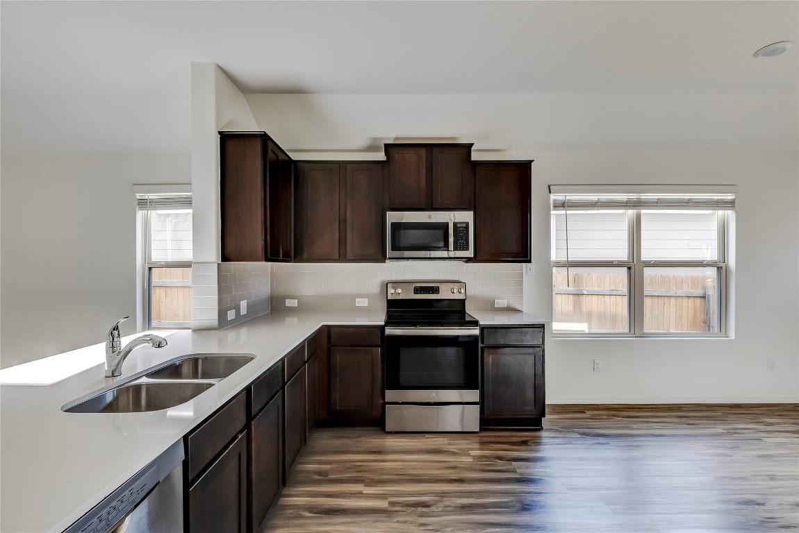 545 Greatest Gift Way Jarrell, TX 76537 - Photo 13 of 34 Kitchen featuring stainless steel appliances, dark brown cabinets, dark wood-style flooring, light stone countertops, and decorative backsplash