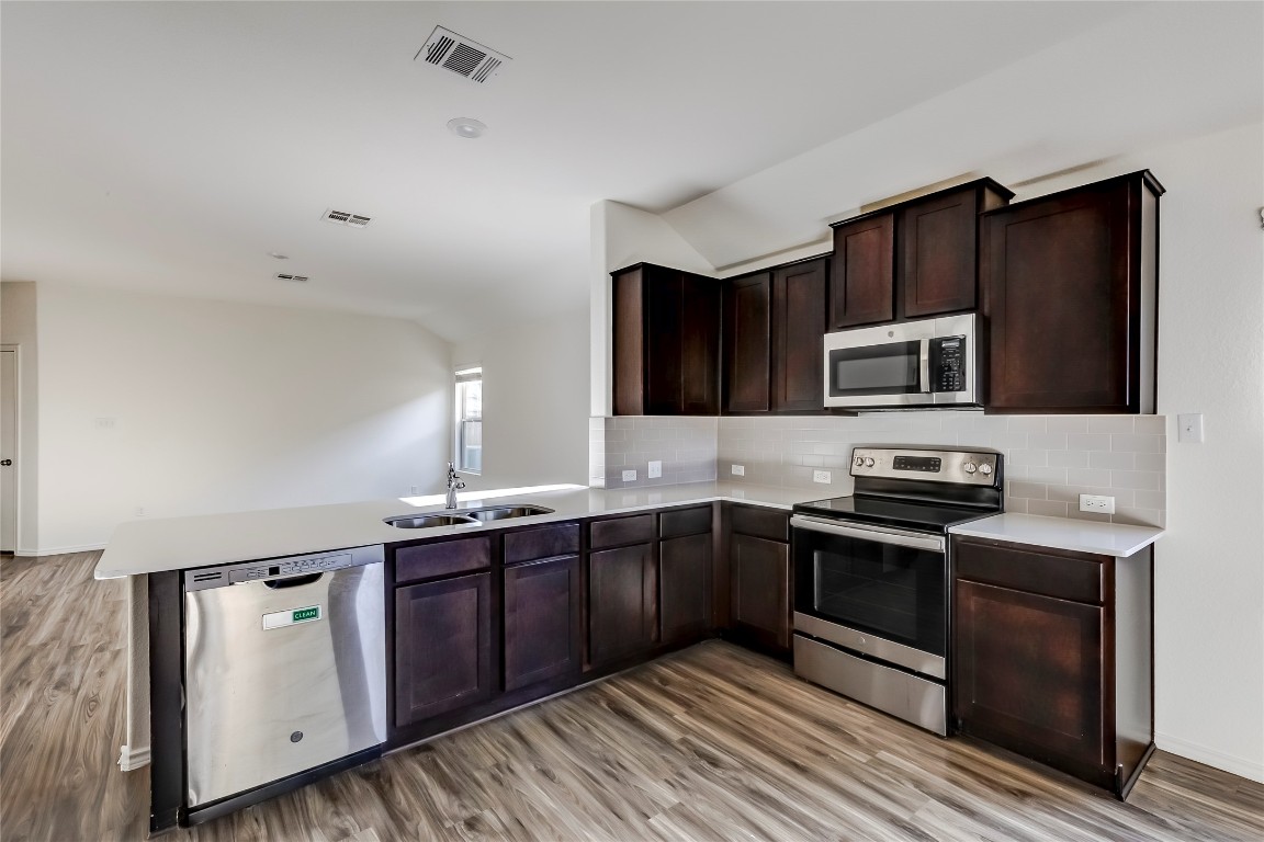 545 Greatest Gift Way Jarrell, TX 76537 - Photo 14 of 34 Kitchen featuring appliances with stainless steel finishes, dark brown cabinets, a peninsula, and light wood-style floors