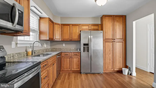 a kitchen with granite countertop wooden floors stainless steel appliances a sink and a window