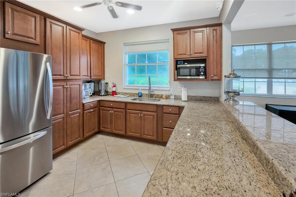 6899 Rain Lily Road, Unit 103 Naples, FL 34109 - Photo 37 of 39 Kitchen featuring stainless steel appliances, light stone counters, wood finish cabinetry, and ceiling fan