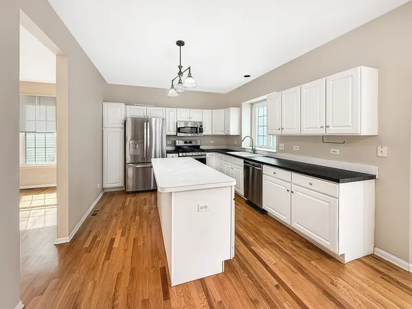 a kitchen with granite countertop wooden floors stainless steel appliances a sink and cabinets