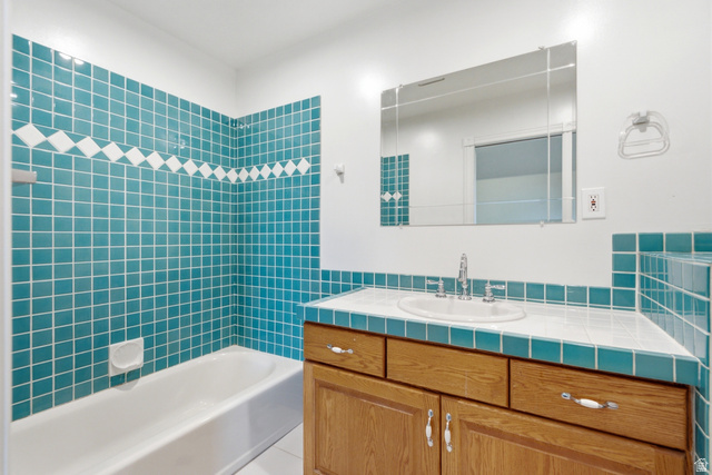 3535 Homestead Road Park City, UT 84098 - Photo 71 of 81 Bathroom featuring bright teal and white square tilework, a white porcelain bathtub, and a wood-finish vanity with a built-in sink
