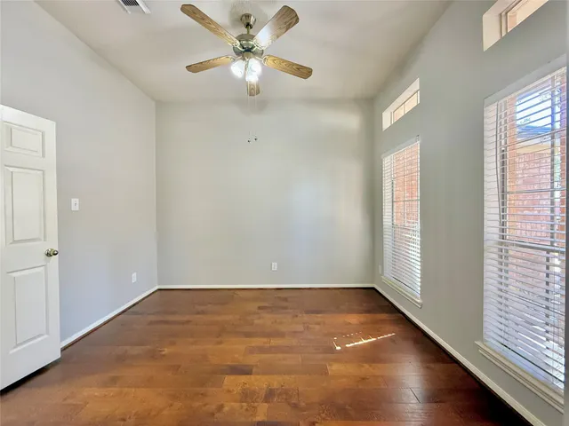 an empty room with wooden floor fan and windows
