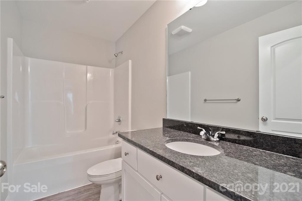 131 Powder Street Southwest Concord, NC 28025 - Photo 15 of 29 a bathroom with a granite countertop sink a toilet a mirror a bathtub and shower