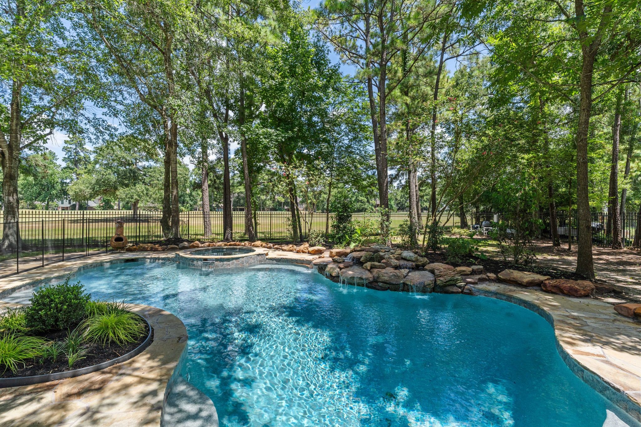 31 Hollymead Drive Spring, TX 77381 - Photo 42 of 50 This backyard features a beautiful, tree-lined pool with a natural rock border, a heated spa with a waterfall feature creating a serene, private oasis perfect for relaxation and entertaining.