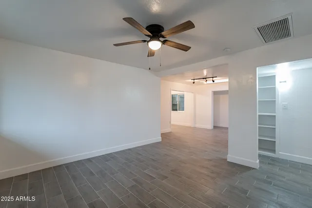 a view of an empty room with wooden floor and a ceiling fan