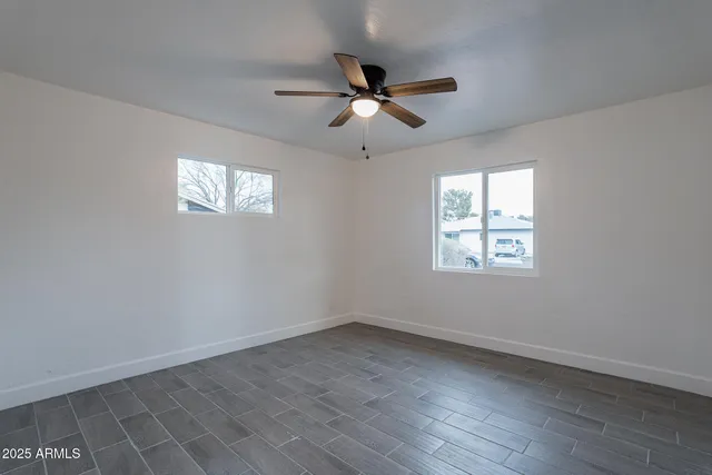 an empty room with wooden floor ceiling fan and windows