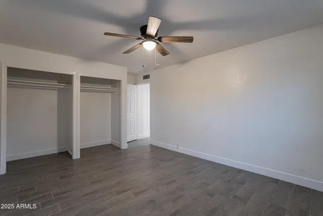 an empty room with wooden floor fan and windows
