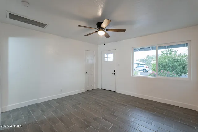 an empty room with wooden floor fan and windows