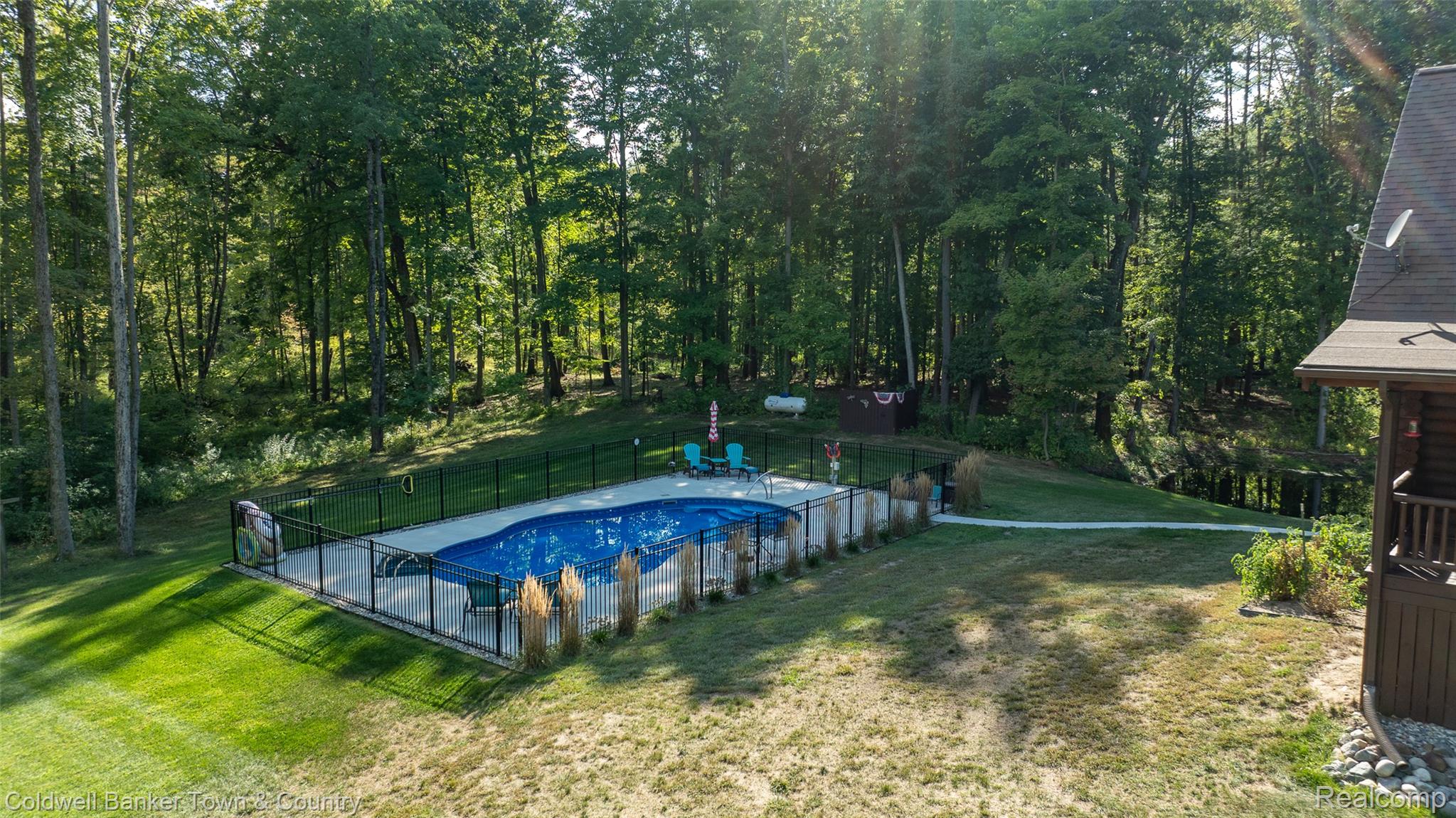 7023 Munsell Road Howell, MI 48843 - Photo 9 of 55 Expansive backyard featuring a fenced-in swimming pool with a concrete surround, mature trees, and a manicured lawn