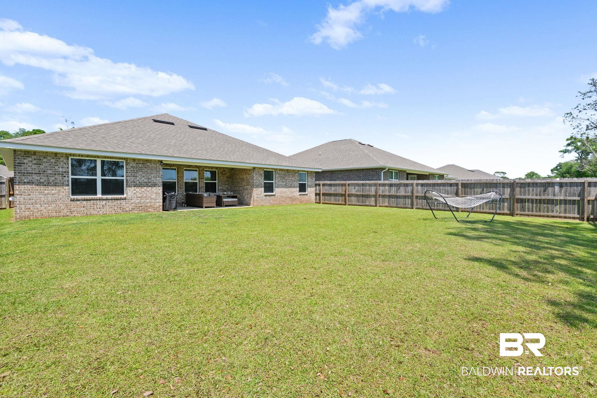 8021 Valor Rdg Way North Mobile, AL 36619 - Photo 7 of 34 Expansive fenced backyard featuring a manicured lawn, brick exterior, and a covered patio area with a concrete surface