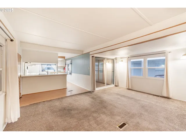 a view of an empty room with kitchen and window