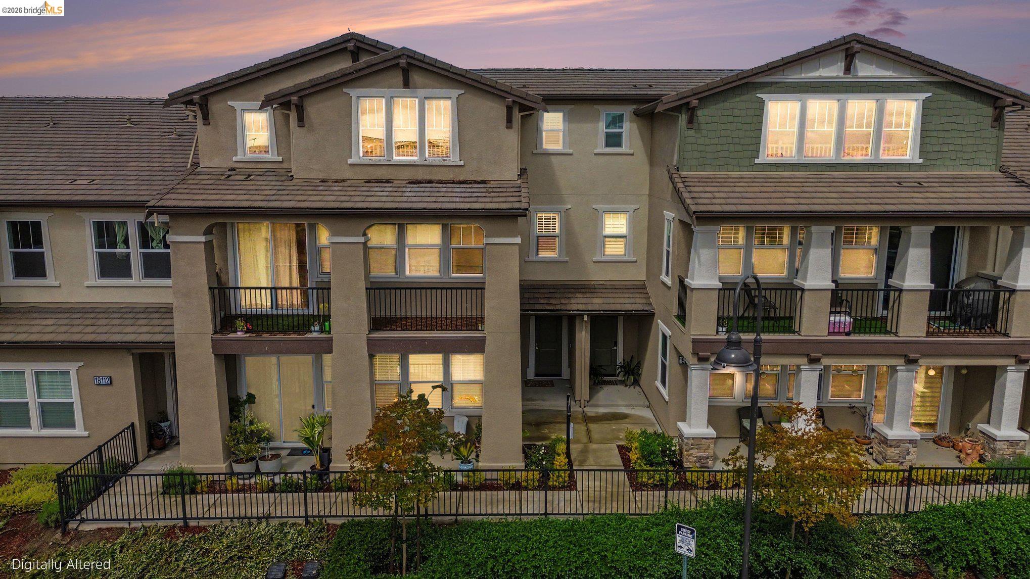 Multi-story townhome exterior featuring an attached balcony, a lower-level patio, and a covered entry